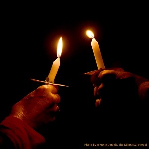 Two peoples' hands, holding lit candles